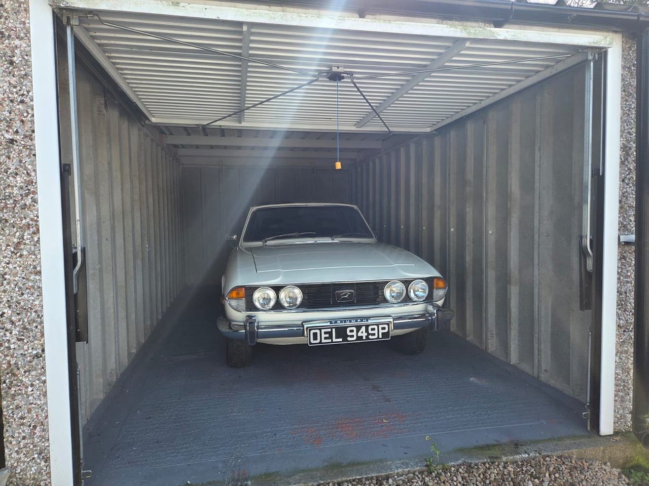 Triumph White Stag, registration OEL 949P, parked nose-out in a concrete garage with a corrugated roof.